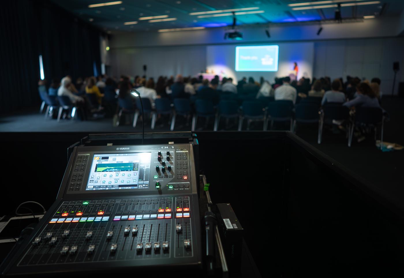 A mixing board in the foreground, being used to control what's happening on stage in the background.