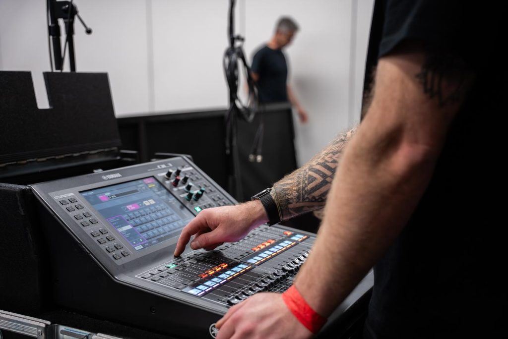 A person pressing a button on a digital sound/lighting mixing board commonly used in event production