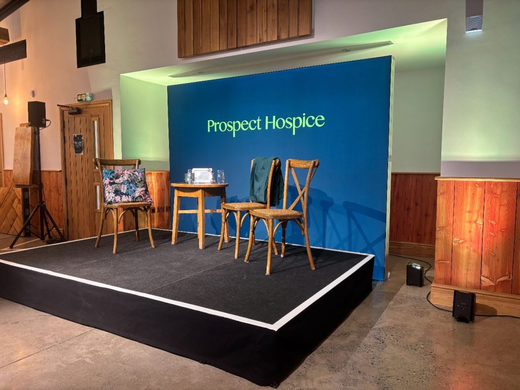 The prospect hospice event stage, with a few chairs for the presenters, and a branded backdrop.