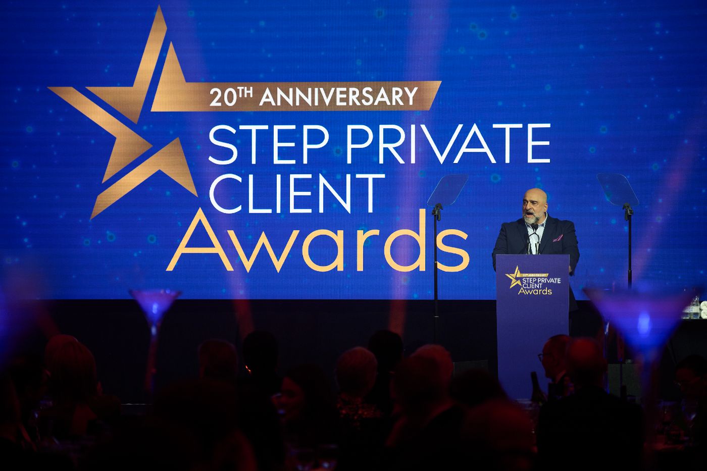 A man on stage, stood at a podium. He is stood in front of a screen that says STEP private client awards.