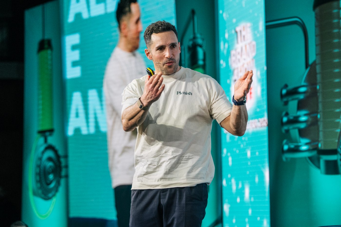 A man gesturing as he presents at a live event.