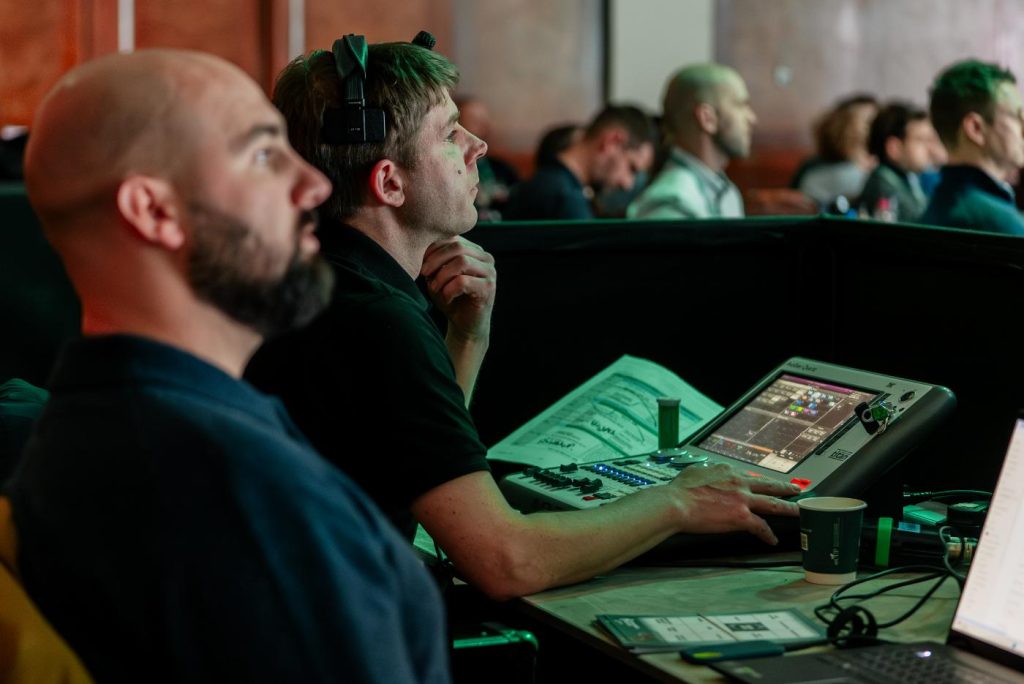 Two event production technicians watching an event, whilst sat behind their equipment.