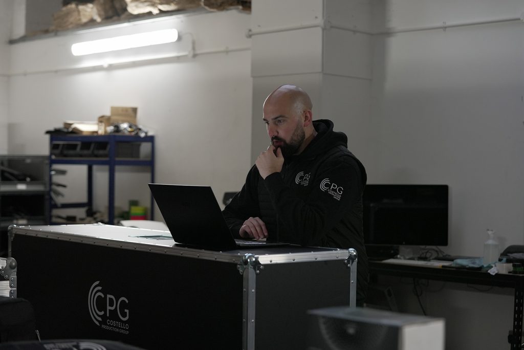 An event manager sat, looking at his laptop that is sat on top of a flight case