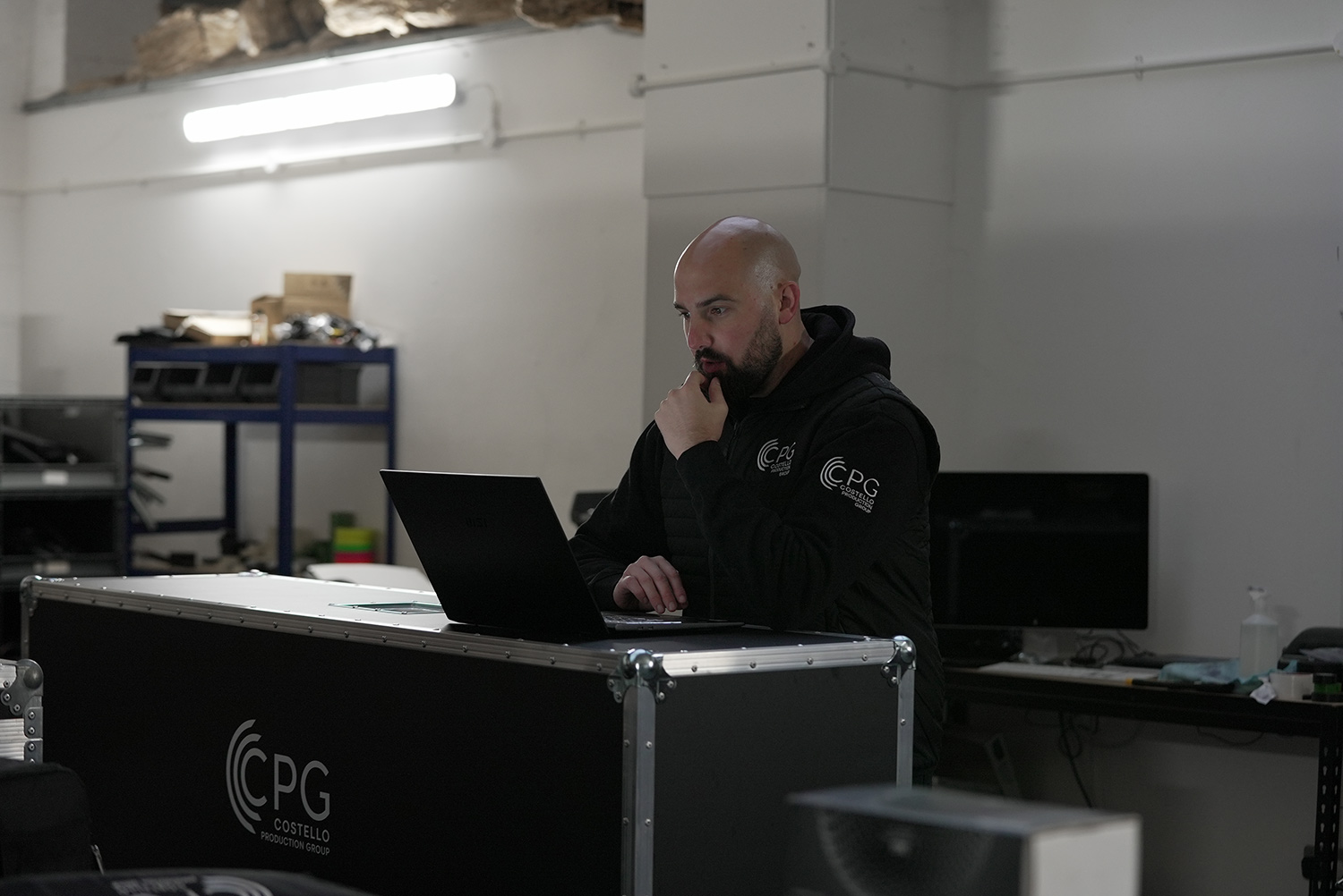 An event manager sat, looking at his laptop that is sat on top of a flight case